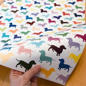 Close-up of a sheet of dacshund (weiner dog) wrapping paper, printed with a pattern of solid-colored dog silhouettes.