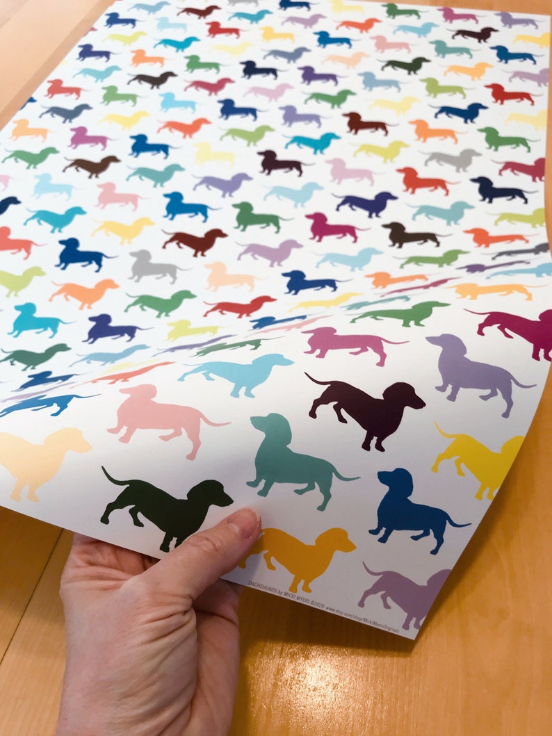 Close-up of a sheet of dacshund (weiner dog) wrapping paper, printed with a pattern of solid-colored dog silhouettes.