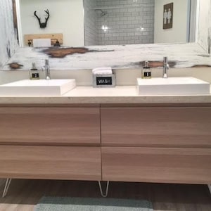 May include: A white bathroom vanity with two sinks and a white countertop. The vanity has four drawers and is supported by hairpin legs. The countertop has a sign that says "WASH" on it.
