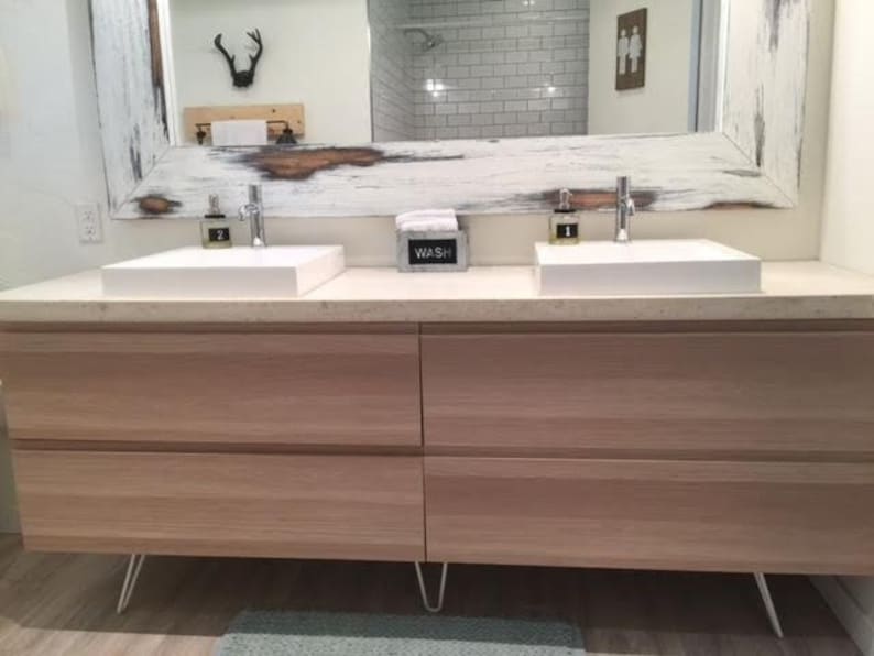 May include: A white bathroom vanity with two sinks and a white countertop. The vanity has four drawers and is supported by hairpin legs. The countertop has a sign that says "WASH" on it.