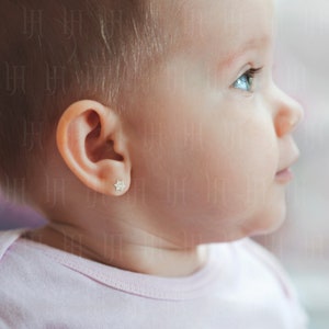 May include: A close-up of a baby's ear with a small, gold, star-shaped earring with clear stones.