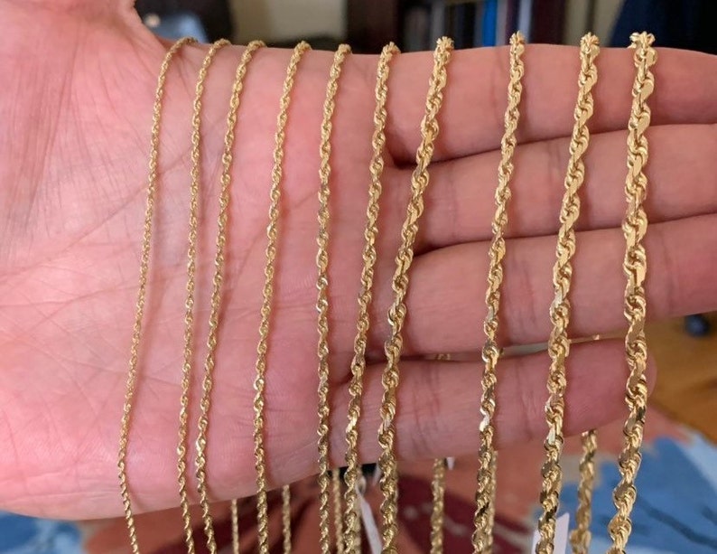 May include: A set of nine gold rope chains of varying thicknesses, displayed on a hand.