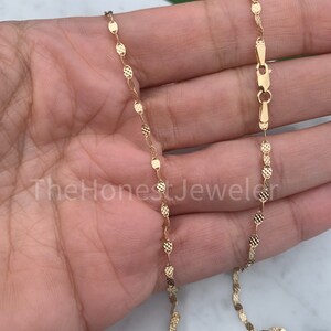 May include: A gold chain necklace with a delicate, textured, oval-shaped link design. The chain is approximately 18 inches long and has a lobster claw clasp.