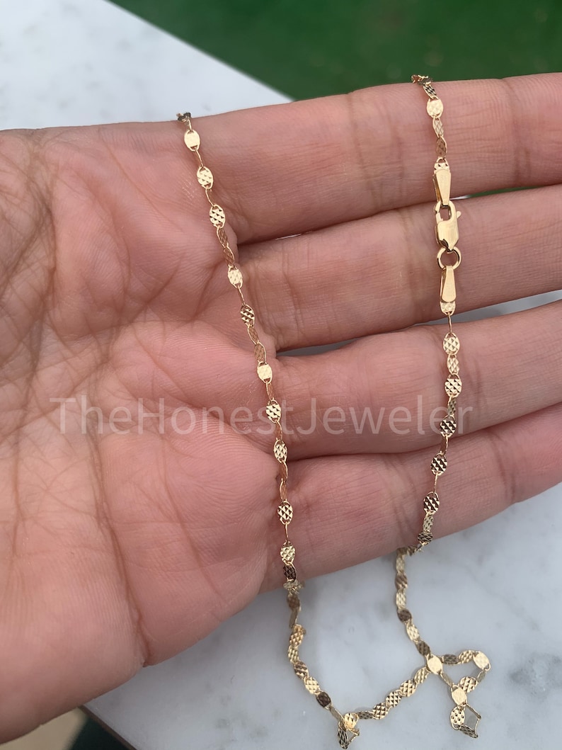 May include: A gold chain necklace with a delicate, textured, oval-shaped link design. The chain is approximately 18 inches long and has a lobster claw clasp.