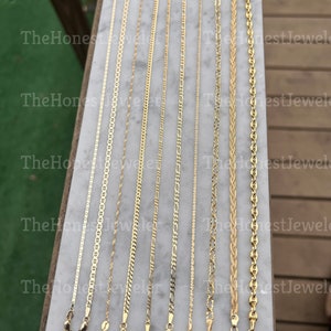 May include: Nine gold chains of different styles and lengths on a white surface. The chains are all made of gold and have a variety of different links.
