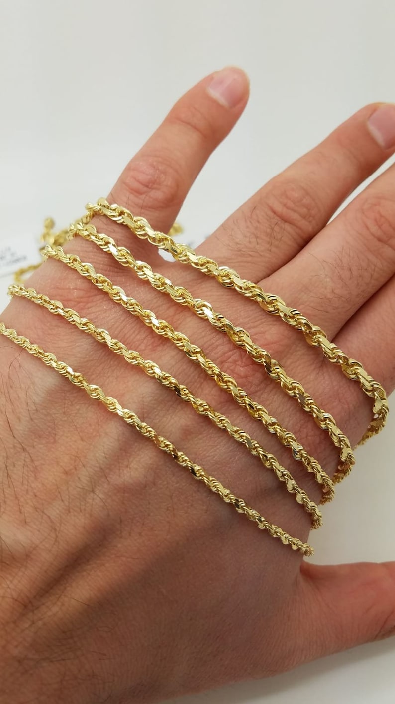 May include: A set of six gold rope chains of varying thicknesses, displayed on a hand.