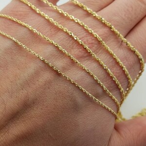 May include: A close-up of a hand holding a variety of gold rope chains. The chains are arranged in order of thickness, with the thinnest chain at the top and the thickest chain at the bottom.
