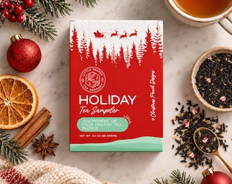 May include: A rectangular box of Holiday Tea Sampler featuring a red background with white silhouettes of a sleigh, reindeer, and pine trees. The text reads Little Prayer Tea Company, Holiday Tea Sampler, and Net Wt: 2.4 oz (68 grams).