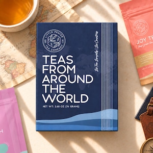 May include: A rectangular dark blue box labeled Little Prayer Tea Company Teas From Around The World with a net weight of 2.68 ounces. The box features white text, a circular logo, and a map graphic, indicating six tea samples included.