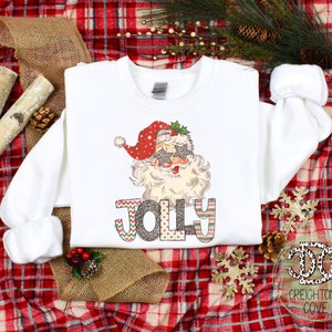 May include: White Christmas sweatshirt with a graphic of Santa Claus wearing sunglasses and the word "Jolly" in colorful letters.