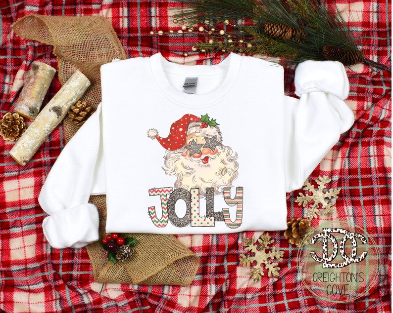 May include: White Christmas sweatshirt with a graphic of Santa Claus wearing sunglasses and the word "Jolly" in colorful letters.