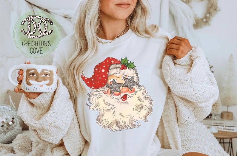 May include: White sweatshirt with a vintage-style illustration of Santa Claus wearing sparkly star-shaped sunglasses. The illustration is in red, white, and green.