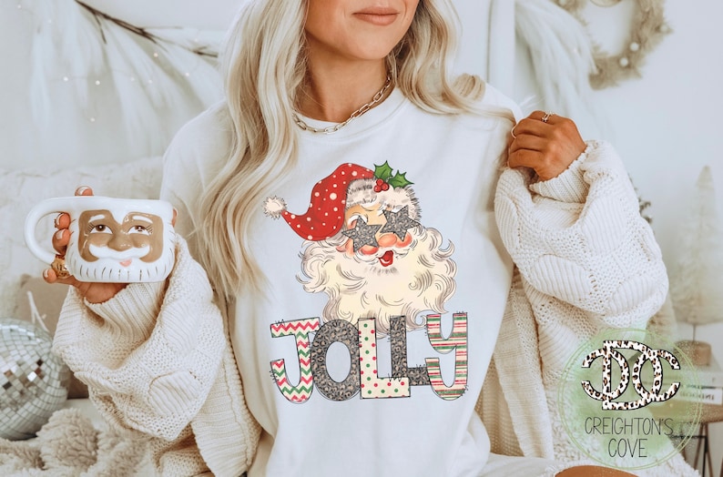 May include: White sweatshirt with a festive design featuring a cartoon Santa Claus wearing sunglasses and the word "Jolly" in colorful patterned letters.