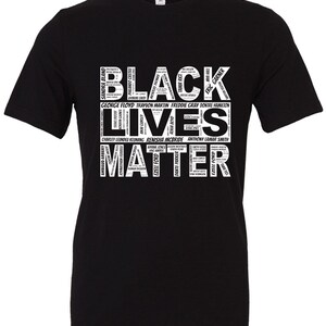 May include: Black t-shirt with the words "Black Lives Matter" in white text. The words are arranged in a way that forms a heart shape. The names of people who have died due to police brutality are listed below the words.