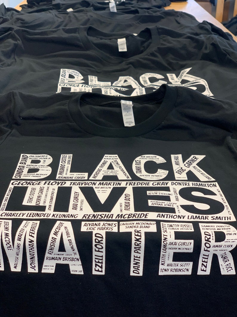 May include: Black Lives Matter t-shirt with a white print of names of people who have been killed by police brutality. The names are arranged in a circle around the words "Black Lives Matter".