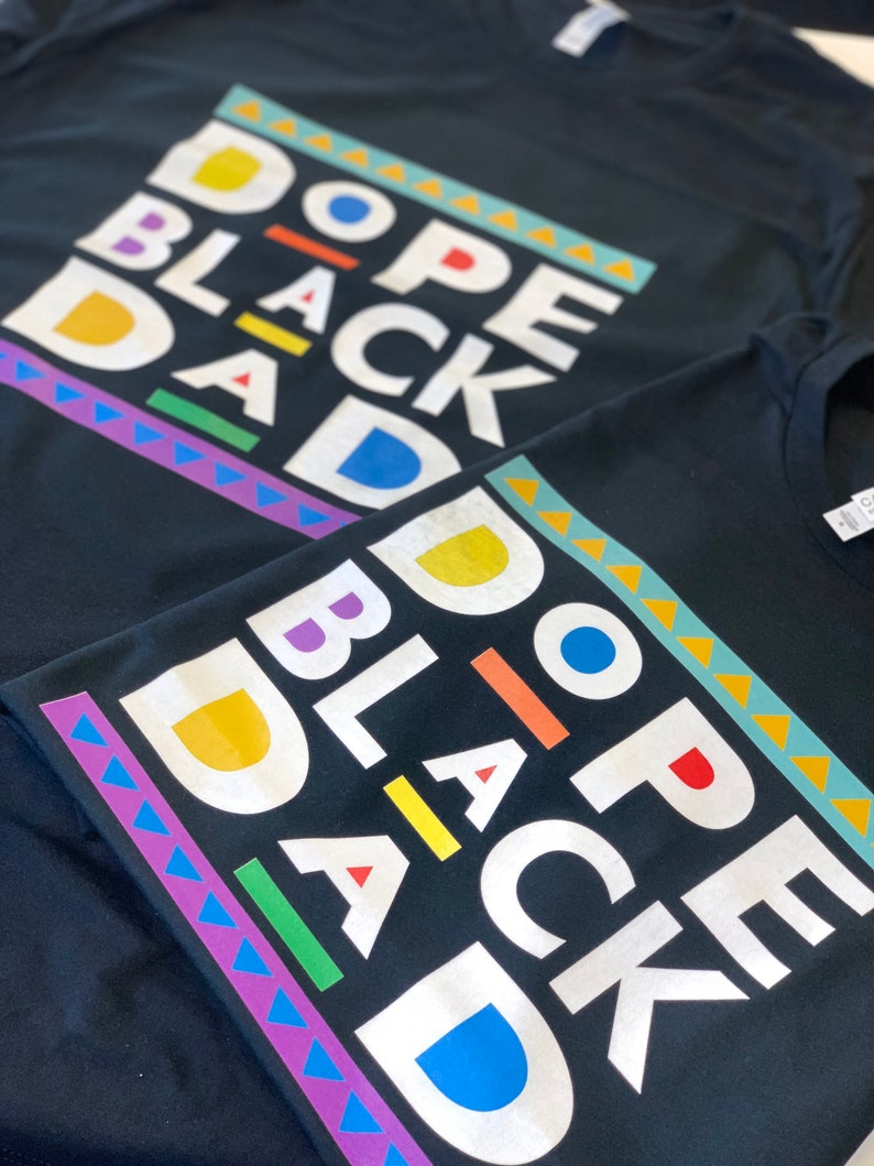 May include: Two black t-shirts with the text "Dope Black Dad" printed in white with colourful accents. The text is in a blocky, retro font.
