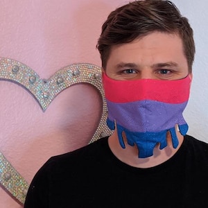 Op de afbeelding: Een persoon draagt ​​een gezichtsmasker met een druppelontwerp in de kleuren van de biseksuele pride-vlag: roze, paars en blauw.