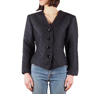 Puede incluir: Una chaqueta acolchada negra con cuello en V y cuatro botones negros. La chaqueta tiene una silueta ajustada y mangas largas.