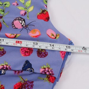 May include: A light blue fabric with a colorful pattern of butterflies, strawberries, and other fruits. A measuring tape shows a length of approximately 16 inches. The fabric has a blue trim.