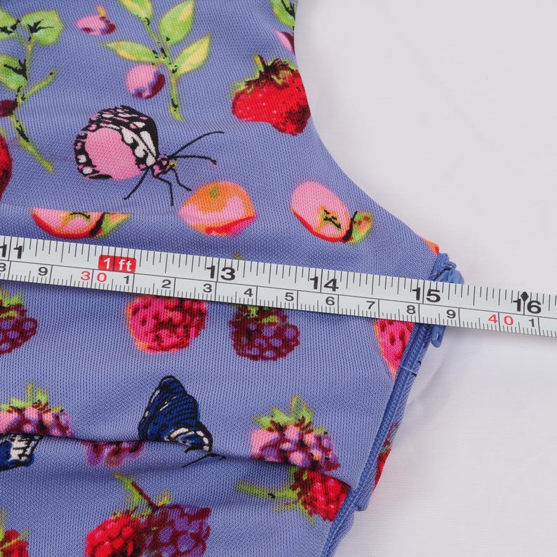 May include: A light blue fabric with a colorful pattern of butterflies, strawberries, and other fruits. A measuring tape shows a length of approximately 16 inches. The fabric has a blue trim.