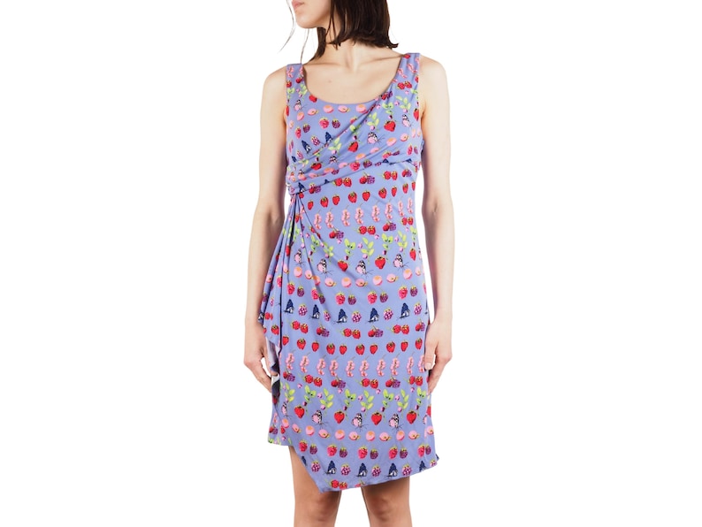 May include: A sleeveless, knee-length dress in a light purple hue, adorned with a playful pattern of strawberries, cherries, and other fruit motifs. The dress features a draped design at the neckline and waist, adding a touch of elegance to the casual style.