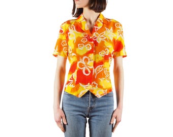 May include: A short-sleeved button-down shirt with a vibrant floral pattern in shades of orange, yellow, and white. The shirt has a classic collar and is paired with blue jeans. The floral print adds a tropical flair to the top.