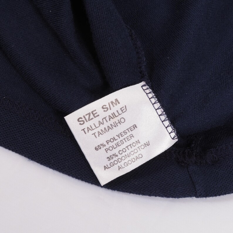 May include: Close-up of a navy blue garment with a white tag. The tag reads "SIZE S/M" and lists the fabric composition as 65% polyester and 35% cotton. The garment's texture is visible.