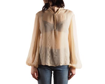 May include: A sheer, light beige blouse with long, voluminous sleeves. The blouse features a high, rounded collar with a row of small, decorative buttons down the front. The fabric has a subtle, vertical striped pattern.