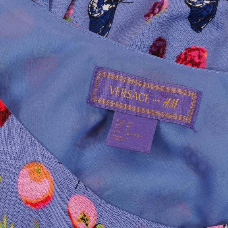 May include: A light blue dress with a floral and butterfly pattern. The dress features a tag with the text "VERSACE for H&M". The tag also includes size information.