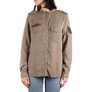 May include: A long-sleeved, olive-green button-down shirt with shoulder epaulets and two chest pockets. The shirt features small patches on the chest and sleeve, and is paired with blue jeans. The shirt has a military-inspired design.