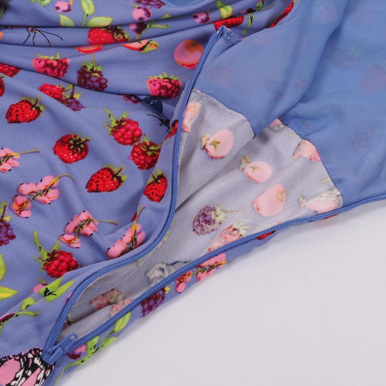 May include: Close-up of a blue dress with a zipper. The dress is adorned with a vibrant pattern of red strawberries, pink flowers, and purple berries. The zipper is a matching blue color, and the fabric appears to be a lightweight material.