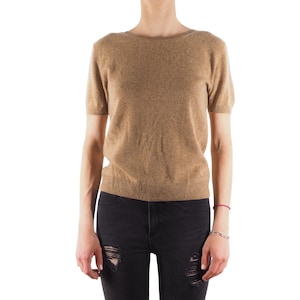 Puede incluir: Un suéter marrón de manga corta con cuello redondo y un ajuste holgado. El suéter se usa sobre jeans negros con detalles desgastados.