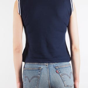 May include: Navy blue sleeveless top with white and light blue trim on the collar and shoulders. The top is paired with light blue denim jeans. The back view shows the details of the top and jeans.