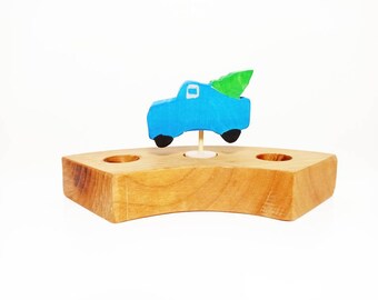 May include: A blue wooden toy truck carrying a green Christmas tree on a wooden base with three holes.