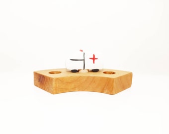 May include: A white toy ambulance with a red cross on the side sits on a wooden base with two holes.