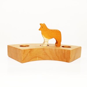 May include: A wooden toy animal, a fox, standing on a wooden base with two holes. The fox is orange and white and the base is light brown.