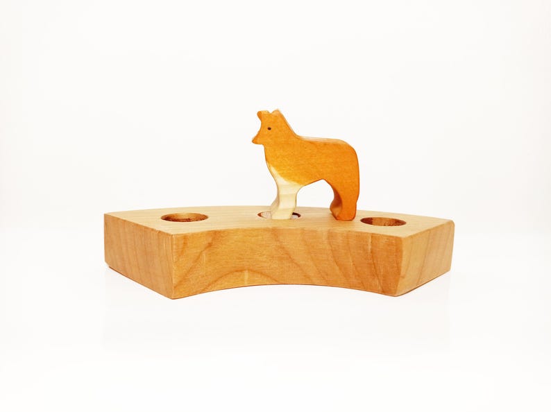 May include: A wooden toy animal, a fox, standing on a wooden base with two holes. The fox is orange and white and the base is light brown.