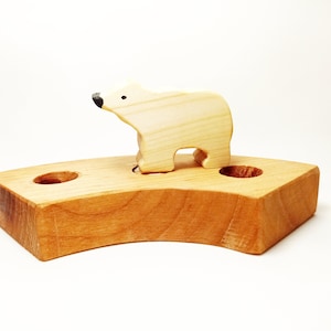 Puede incluir: Un oso polar de juguete de madera de pie sobre una base de madera con dos agujeros. El oso es marrón claro y tiene ojos negros y una nariz negra.