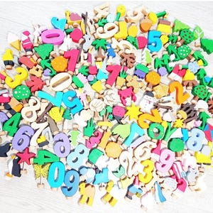 May include: A large collection of colorful wooden numbers and shapes, including trees, stars, and animals. The numbers are painted in various bright colors and are arranged in a random pattern.