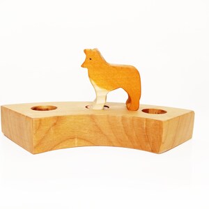 May include: A wooden toy animal, a brown wolf, standing on a wooden base with two holes. The base is shaped like a crescent moon.