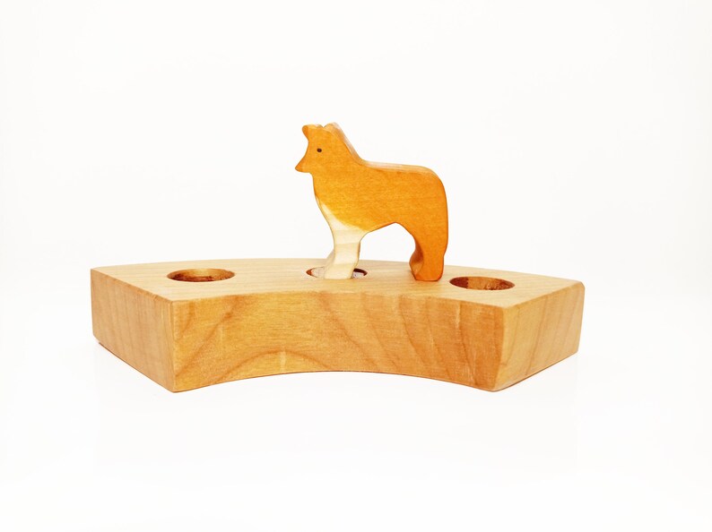 May include: A wooden toy animal, a brown wolf, standing on a wooden base with two holes. The base is shaped like a crescent moon.