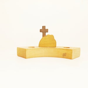 Könnte beinhalten: Holzspielzeug-Set, das einen Hügel mit einem Kreuz auf der Spitze darstellt. Der Hügel ist aus hellbraunem Holz und das Kreuz aus dunkelbraunem Holz. Das Set steht auf einer hellbraunen Holzbasis.