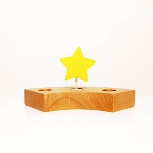 May include: A wooden stand with three holes, shaped like a crescent moon, with a yellow star on top.