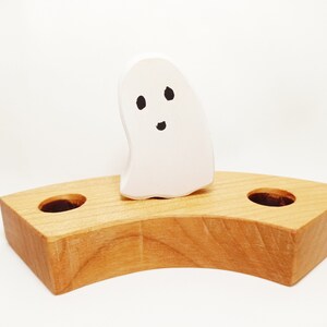 Può includere: Un portacandele in legno a forma di fantasma con due fori per le candele. Il fantasma è bianco con occhi neri e una bocca.