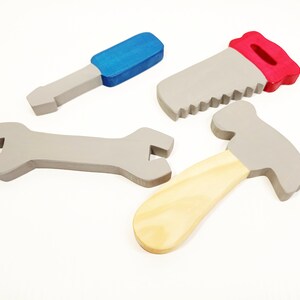 May include: A set of four wooden toy tools, including a hammer, saw, wrench, and screwdriver. The tools are painted in shades of gray, blue, and red.