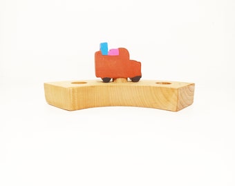 May include: A wooden toy car with a pink, blue, and red paint job sits on a wooden base with two holes. The base is curved and has a natural wood finish.