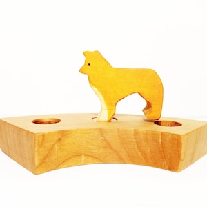 May include: A wooden toy with a yellow dog standing on a wooden base with three holes. The dog is made of wood and has a simple design.