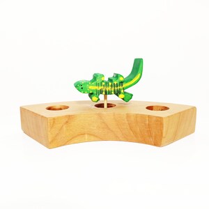 May include: A wooden base with three holes and a green and yellow painted lizard figurine standing in one of the holes.