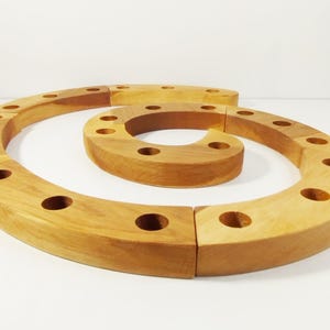 Może przedstawiać: Drewniany świecznik w kształcie spirali z wieloma okrągłymi otworami na świece. Uchwyt wykonany jest z jasnego drewna i składa się z kilku zakrzywionych segmentów. Projekt to dekoracyjny dodatek do domu.