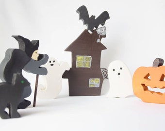 May include: A Halloween themed wooden craft set featuring a witch, a black cat, two ghosts, a haunted house with a bat on top, and a jack-o'-lantern.